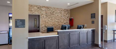 A reception desk with a digital screen, a guest laundry sign, and a business center sign.