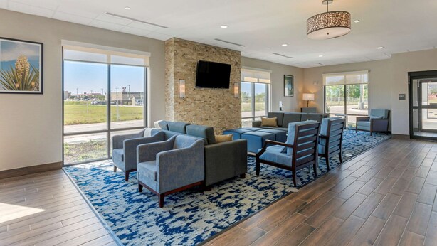 A spacious lobby with a stone accent wall, a flat-screen TV, and a large window offering a view of the outdoors. - Comfort Inn & Suites Balch Springs - SE Dallas (Mesquite)