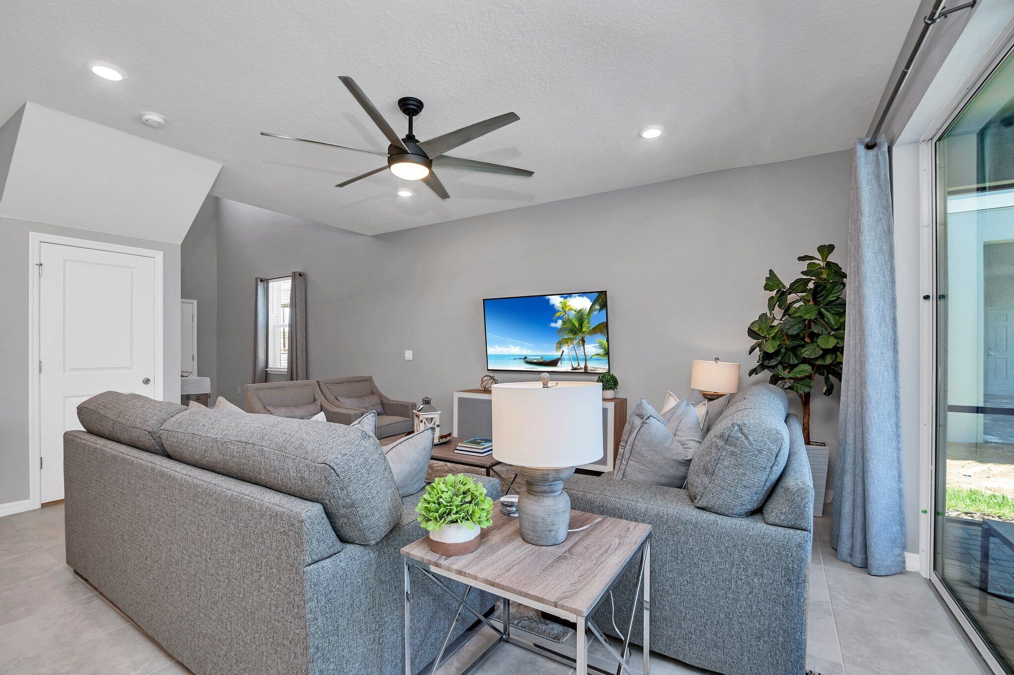 A modern living room with grey sofas, a ceiling fan, a TV, and a plant.
