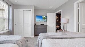 Ein Schlafzimmer mit zwei Betten, einem Fernseher auf einer Kommode und einer Tür zu einem anderen Raum.