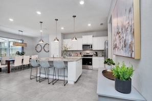 A modern kitchen with white cabinets, a central island with bar stools, pendant lighting, and a large window providing natural light.