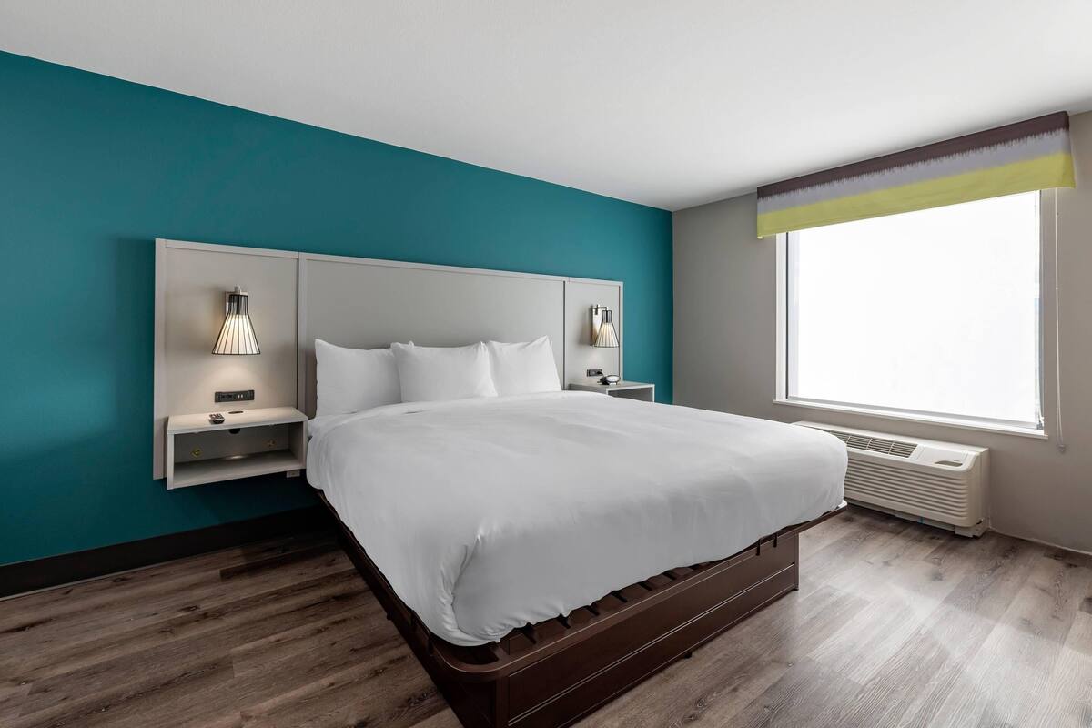 A modern hotel room with a large bed, built-in nightstands, and a window with a view.