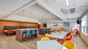 A modern dining area with high ceilings, wooden flooring, and a mix of yellow and orange chairs. - Comfort Suites Colorado Springs East -Medical Center Area (Colorado Springs)