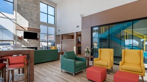 A spacious lobby with a high ceiling, a stone accent wall, a flat-screen TV mounted on the wall, and a staircase with yellow railings. - Comfort Suites Colorado Springs East -Medical Center Area (Colorado Springs)
