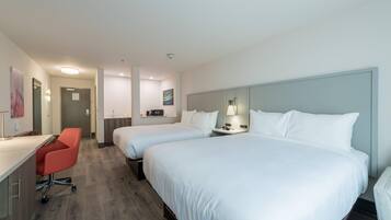 A hotel room with two single beds, a desk with a chair, a small kitchenette, and a bathroom.