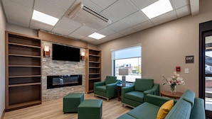 A modern lounge area with a flat-screen TV, green sofas, and a stone accent wall. - Comfort Suites Colorado Springs East -Medical Center Area (Colorado Springs)