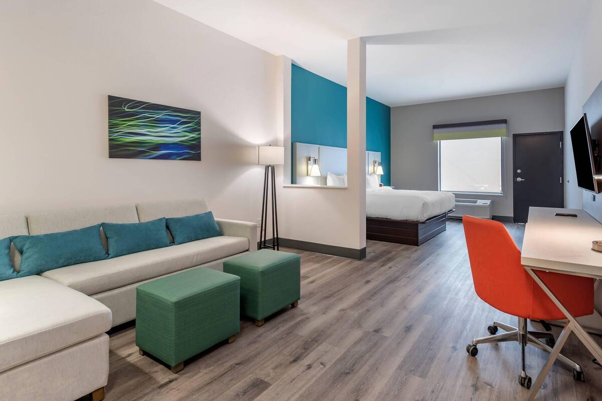 A modern hotel room with a sofa, ottomans, a desk, and a bed.