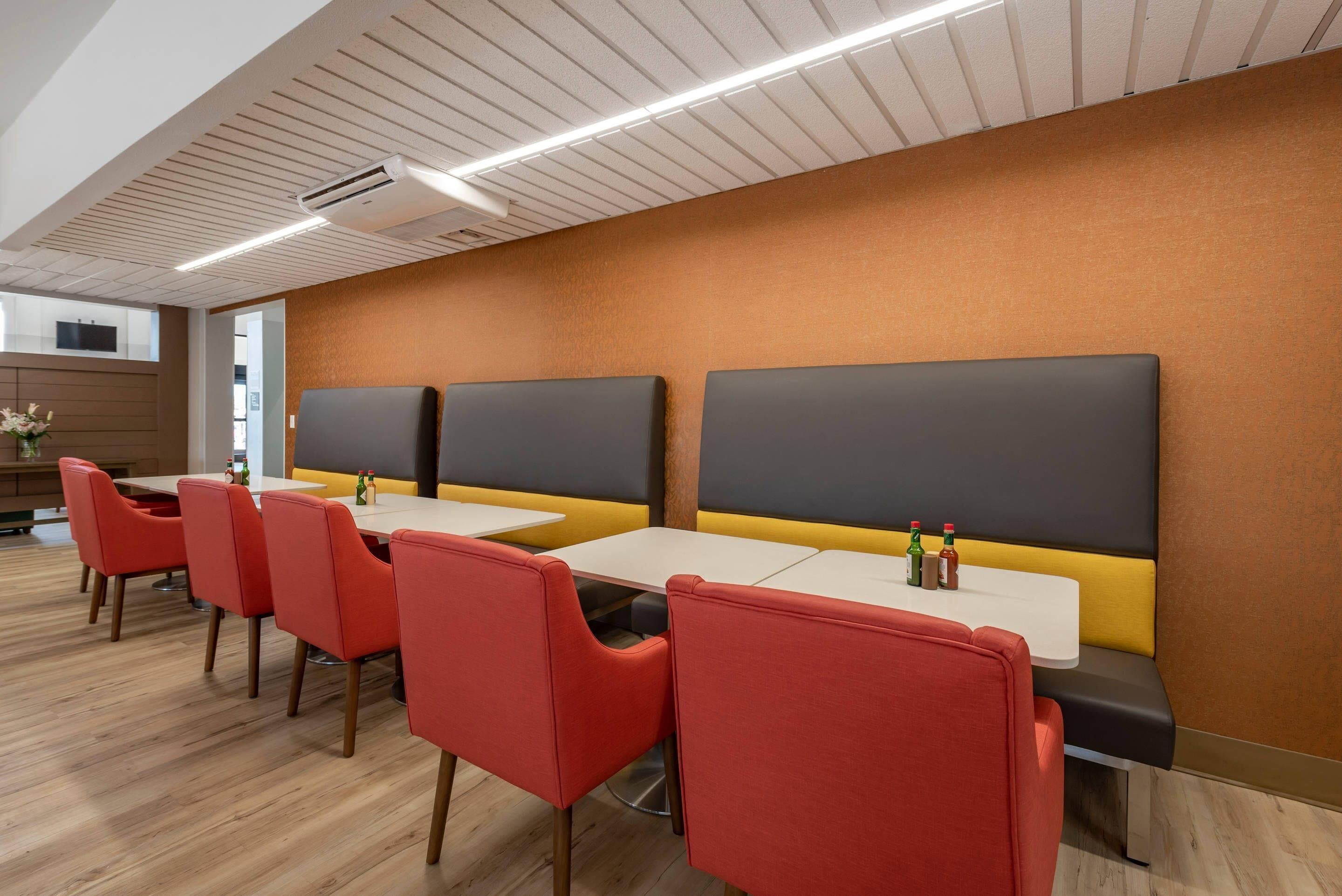 A modern dining area with red chairs, white tables, and black cushioned booths.