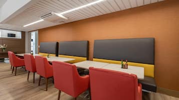 A modern dining area with red chairs, white tables, and black cushioned booths.