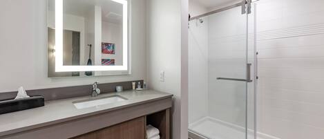 A modern bathroom with a large mirror, a sink, a shower, and wooden cabinets.
