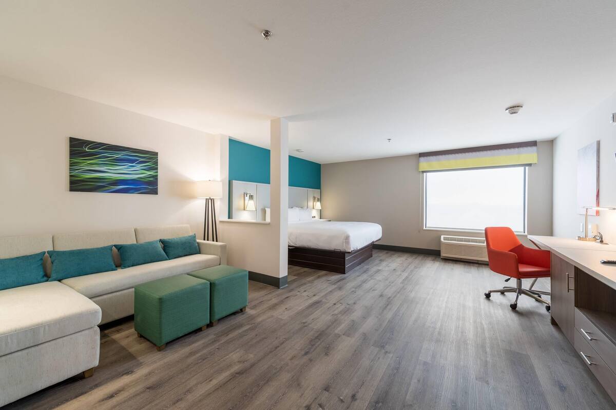 A modern hotel room with a sofa, a bed, a desk, and a window.