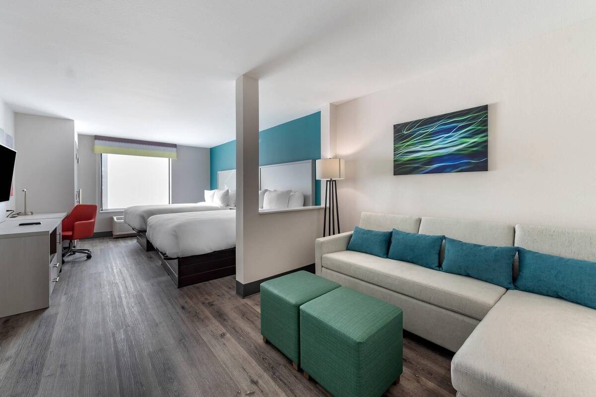 A modern hotel room with a bed, a sofa, a desk, and a chair.