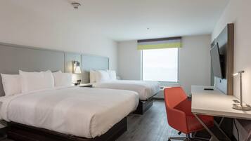 A hotel room with two beds, a desk, a chair, a TV, and a window.