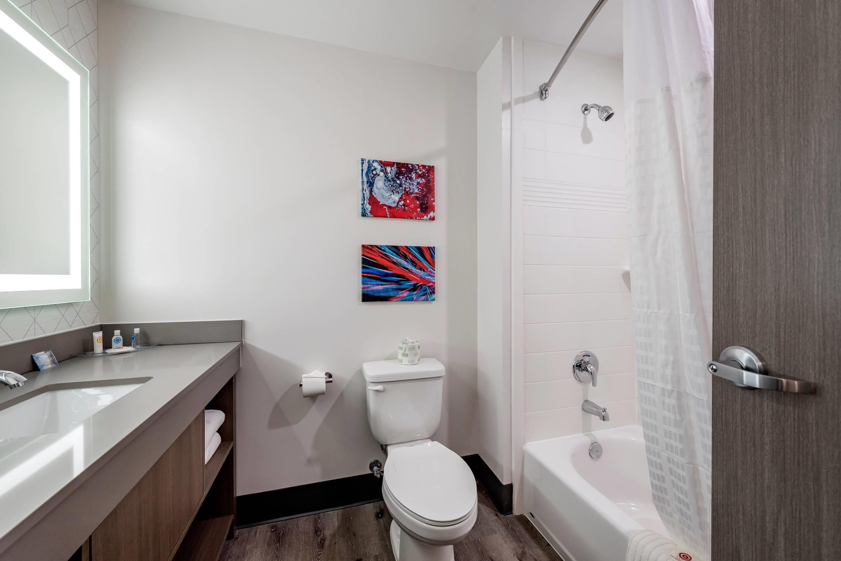 Un baño moderno con un lavamanos, un inodoro y una bañera blancos. Hay dos obras de arte colgadas en la pared y una cortina de ducha.