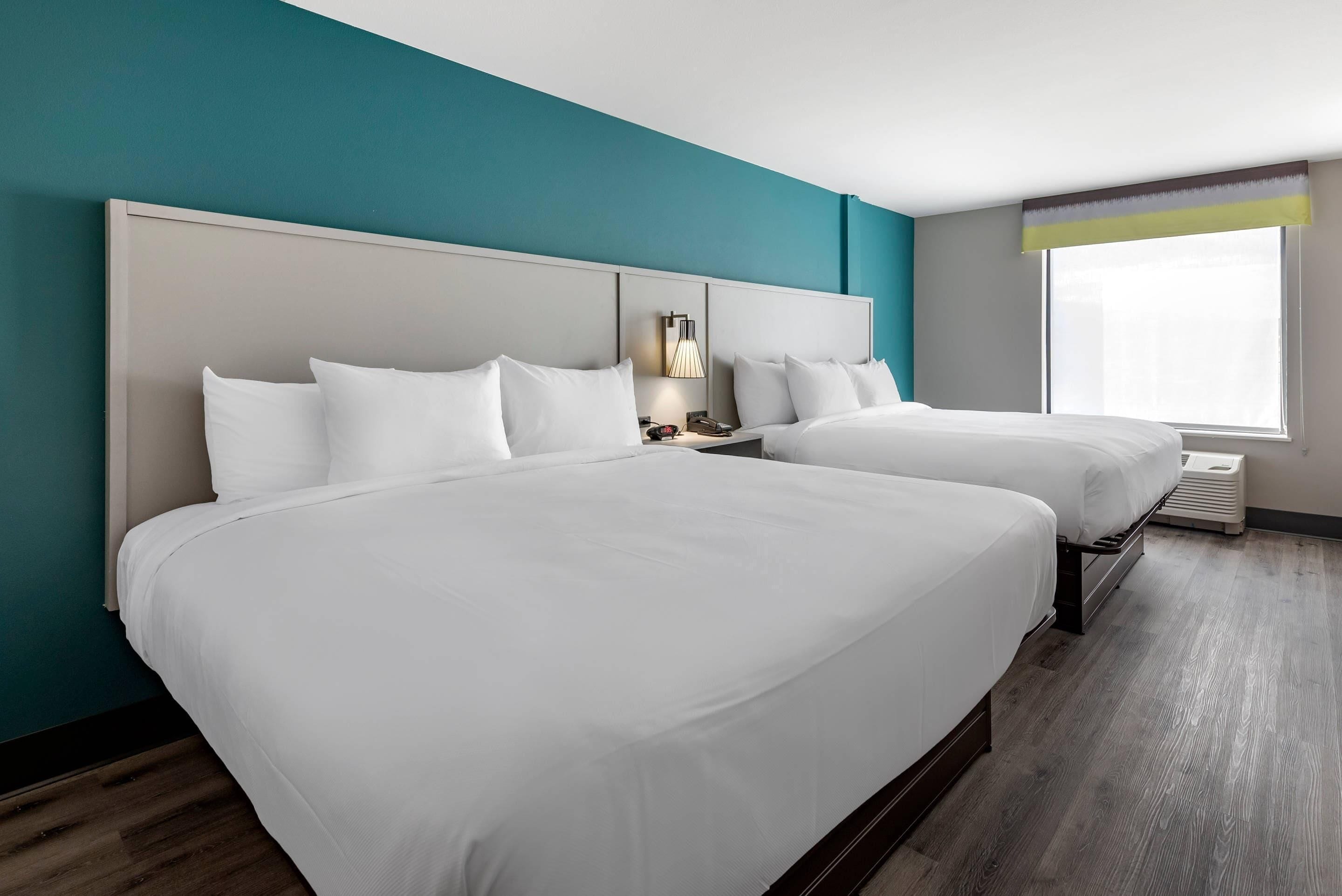 A hotel room with two beds, a nightstand with a lamp, and a window with a view.