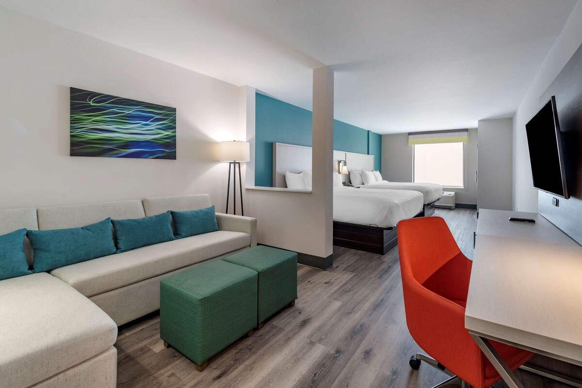 Une chambre d’hôtel moderne équipée d’un canapé, d’un pouf, d’un lit, d’un bureau et d’une télévision.