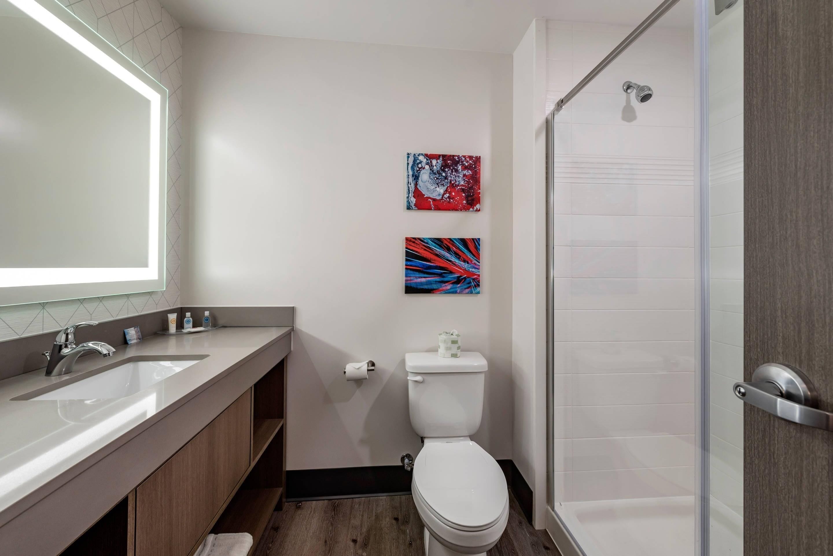 Un baño moderno con un espejo grande, dos lavamanos, un inodoro y una ducha.