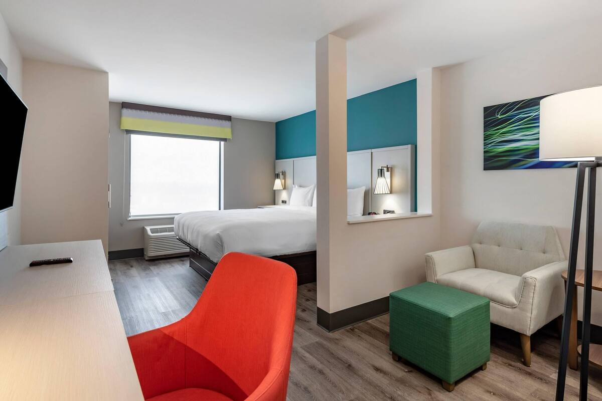 A hotel room with a bed, a desk, a chair, and a green ottoman.