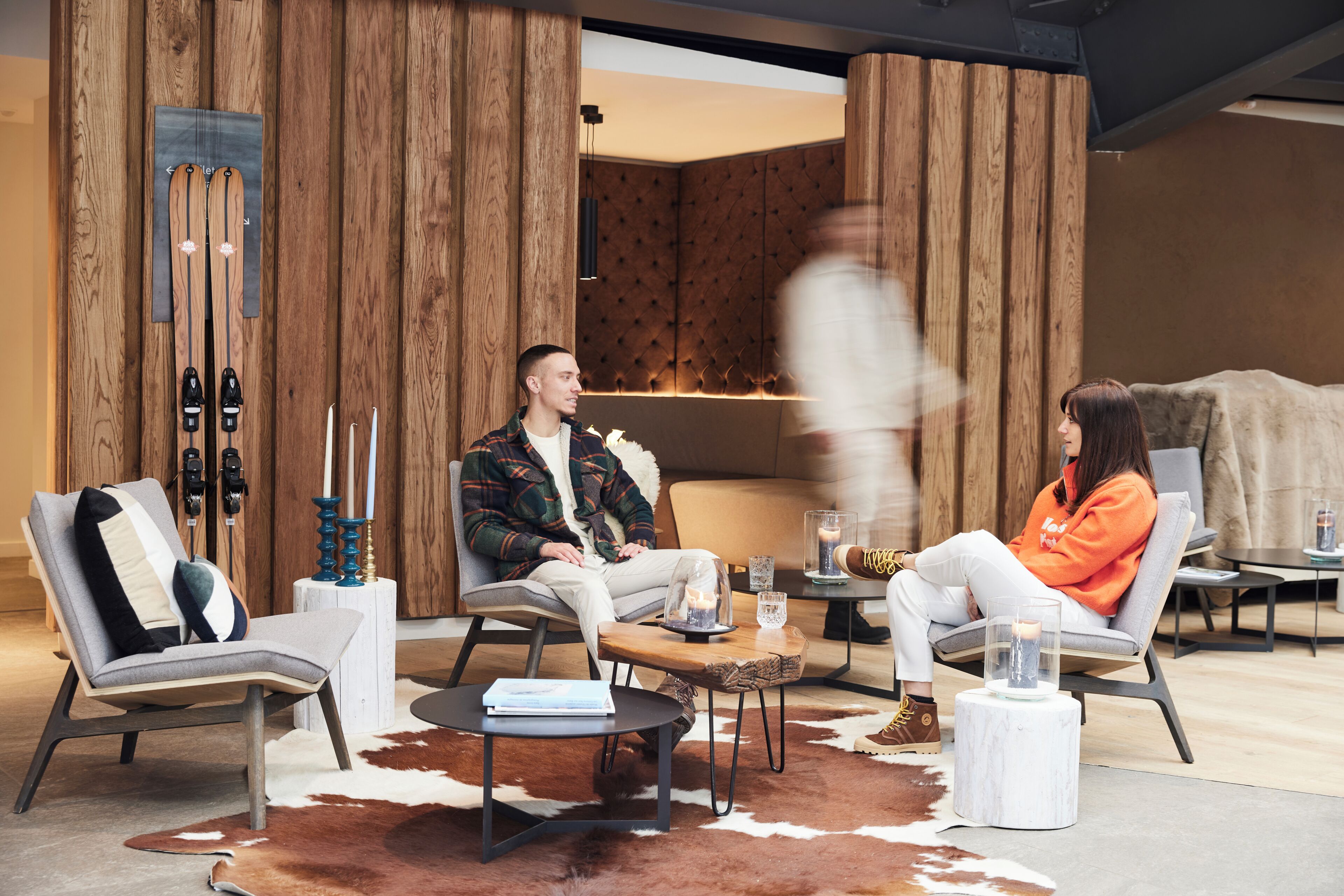 A modern interior with wooden paneling, a ski rack, and a cozy seating area with a cowhide rug.