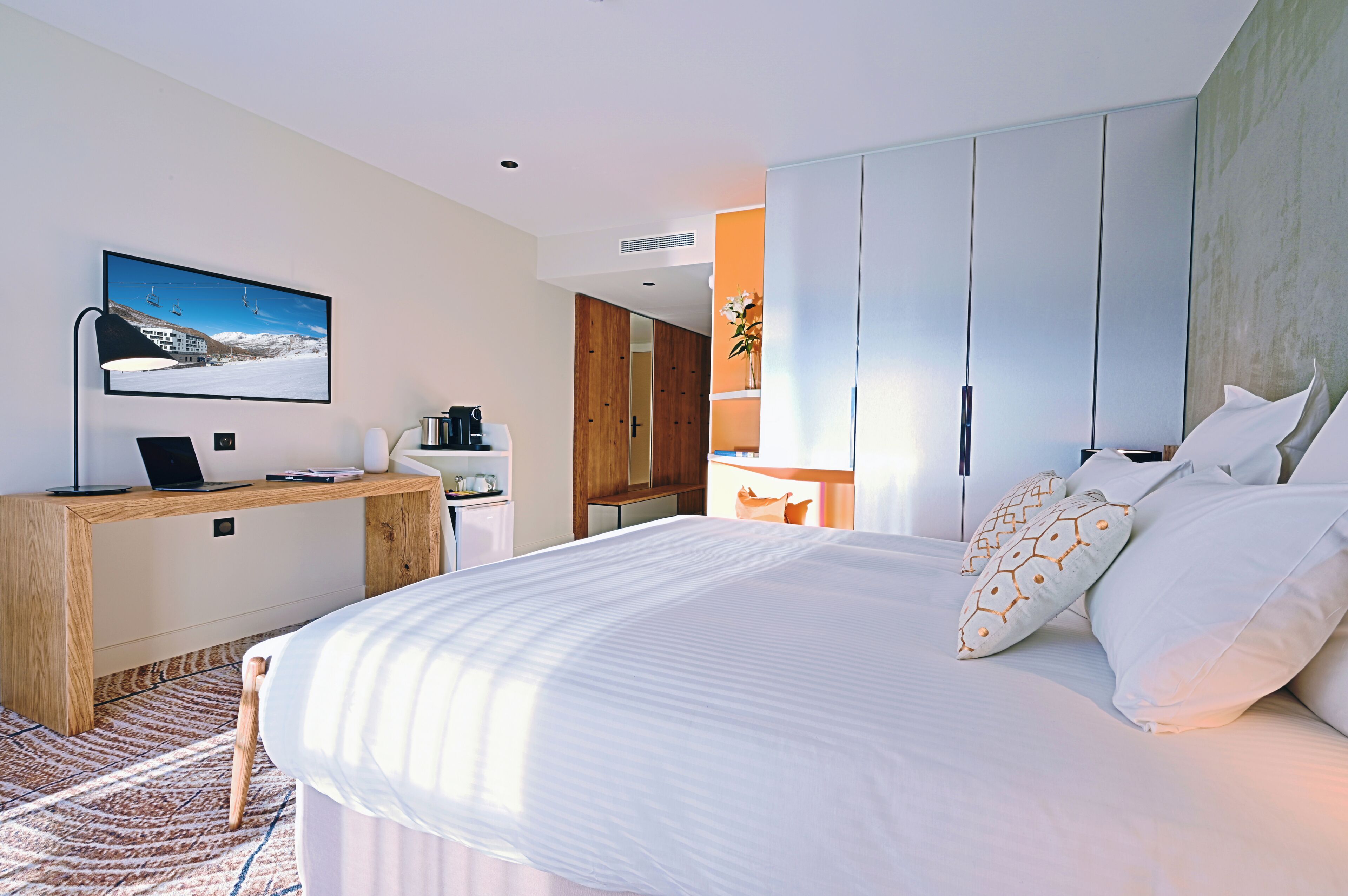 A modern hotel room with a bed, a desk, a television, and a wardrobe.