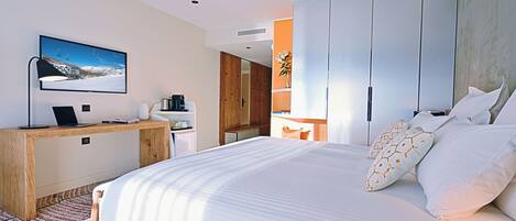A modern hotel room with a bed, a desk, a television, and a wardrobe.