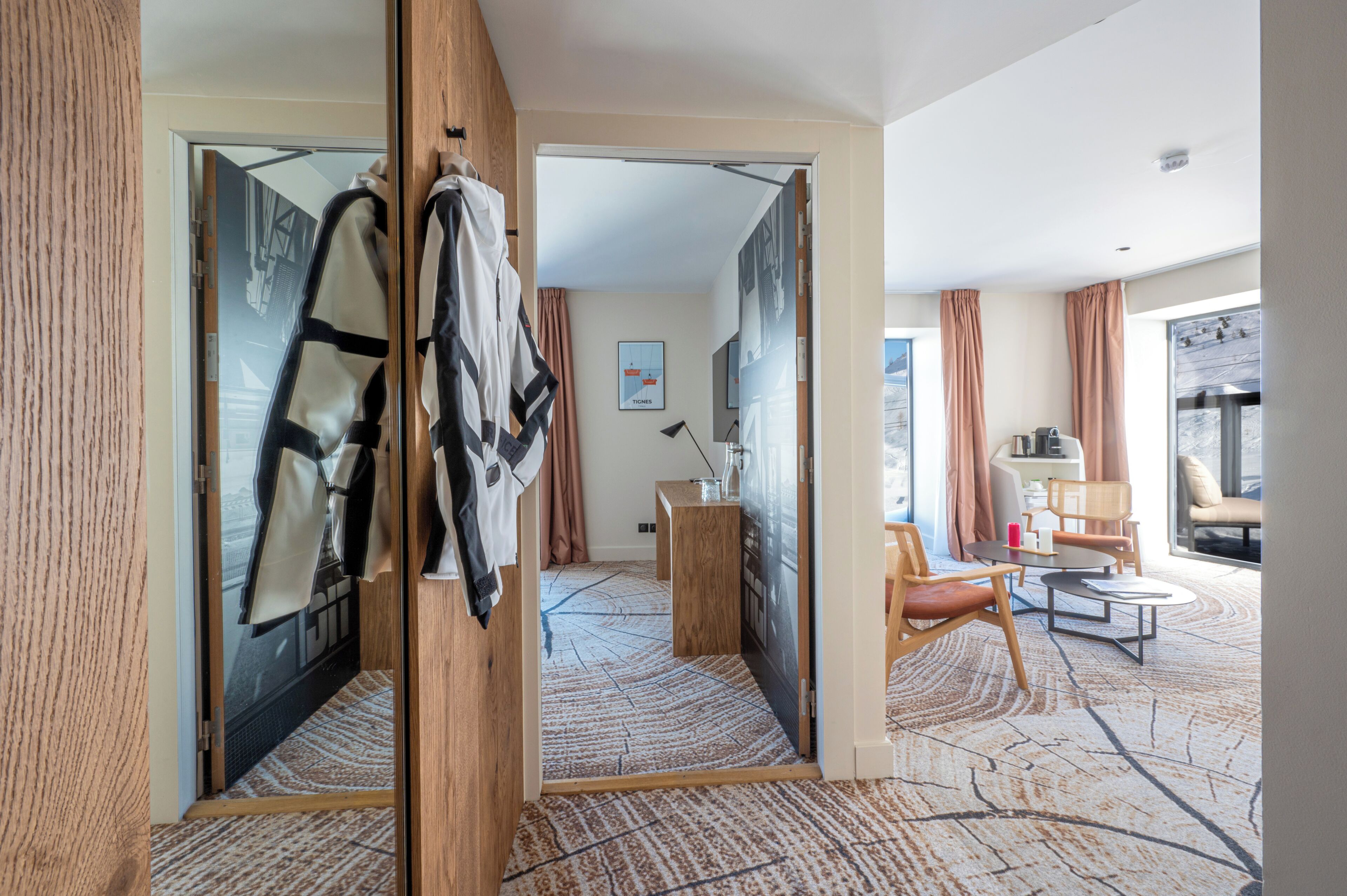 Une chambre d’hôtel dotée d’un grand miroir, d’une armoire en bois, d’un coin salon avec une table et des chaises, et offrant une vue sur l’extérieur.