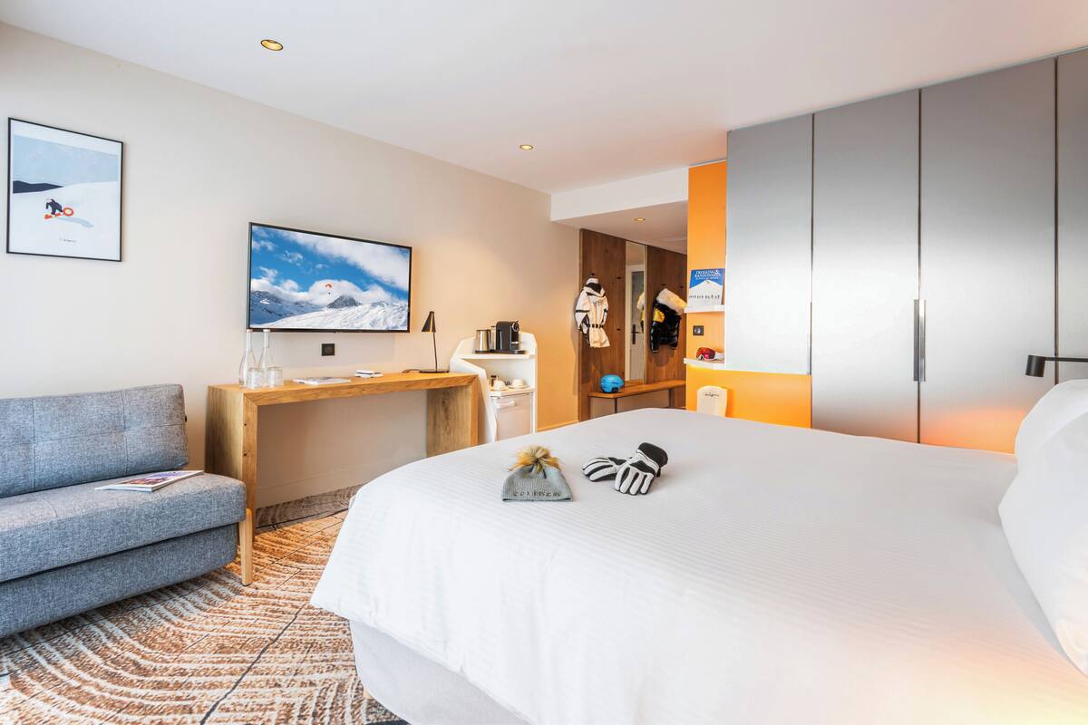A modern hotel room with a bed, a desk, a sofa, and a TV.
