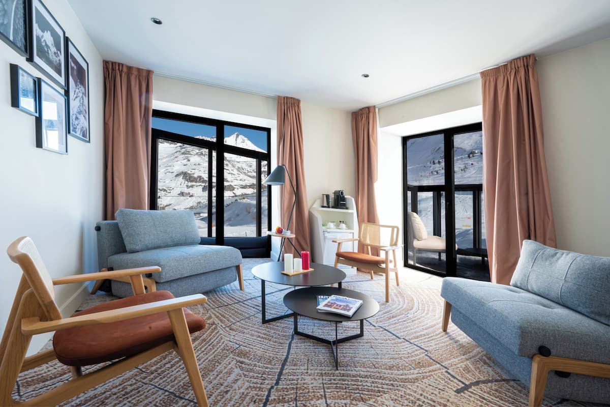 A modern living room with a sofa, chairs, a coffee table, and a view of a snowy mountain.