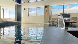 Una piscina interior con vistas a montañas nevadas, un área de descanso con asientos y un diseño arquitectónico moderno.