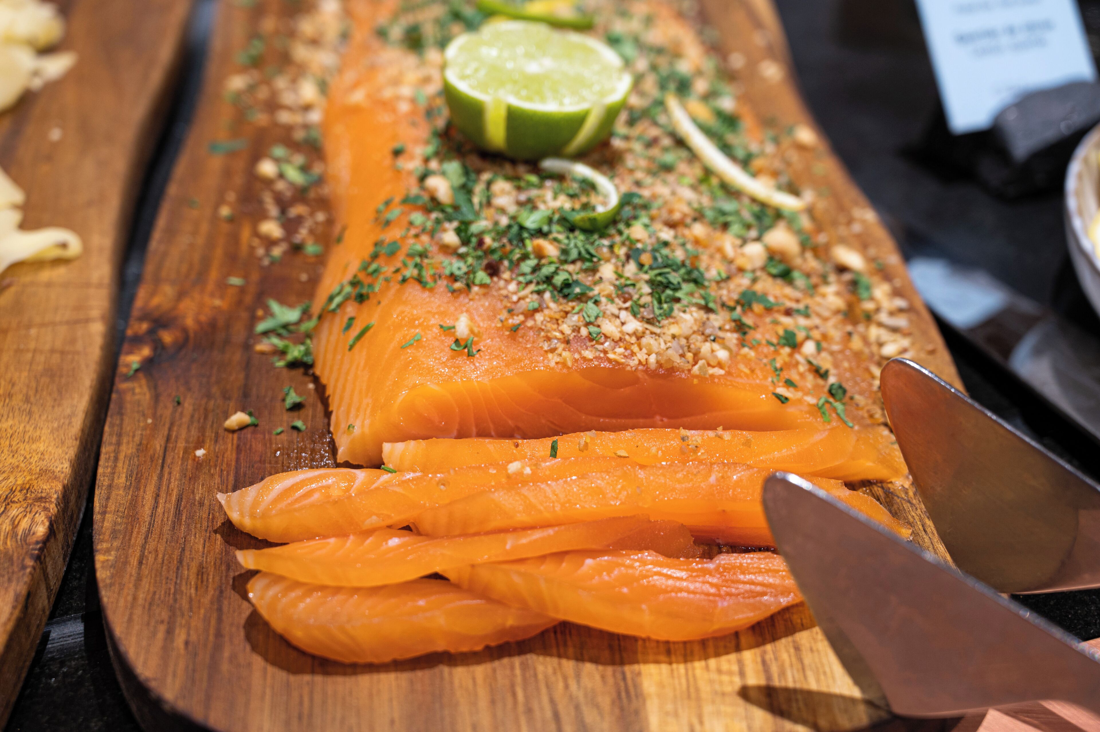 A wooden cutting board with salmon slices, garnished with herbs and lime.