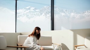 Una persona sentada en un sofá con vistas a la montaña a través de amplias ventanas.