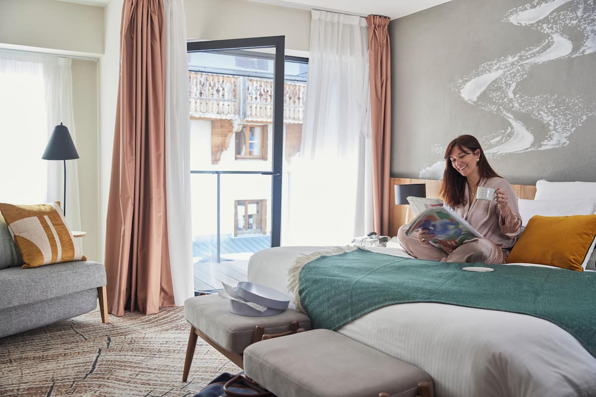 A hotel room with a bed, a sofa, a reading area, and a balcony with a view.