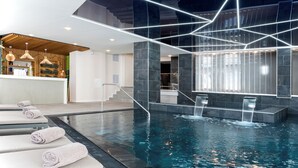 Una piscina interior moderna con una instalación de luces geométricas, una zona de recepción y asientos tipo lounge.