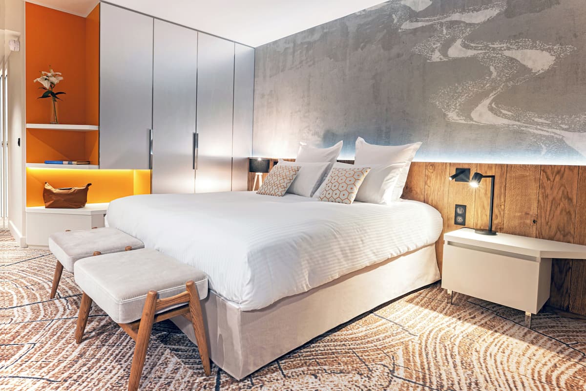A modern bedroom with a large bed, wooden nightstands, a bench, and a wall-mounted shelf with a vase.