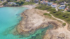 Vista aérea de un pueblo costero con aguas turquesas cristalinas, costas rocosas y una combinación de edificios residenciales.