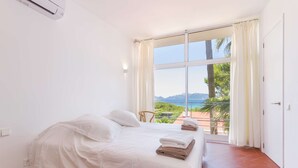 Un dormitorio con cama, vista al mar y balcón con cortinas.