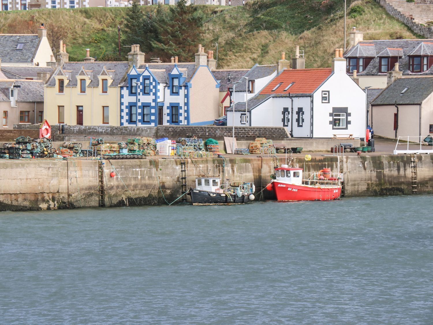 A harbor with boats docked, a stone wall, and colorful buildings in the background.