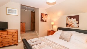 A bedroom with a bed, a wooden dresser, a television, and artwork on the walls. - Harbour View (Buckie)