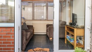 A cozy living room with a sofa, a television on a wooden stand, and a window with blinds. - Harbour View (Buckie)