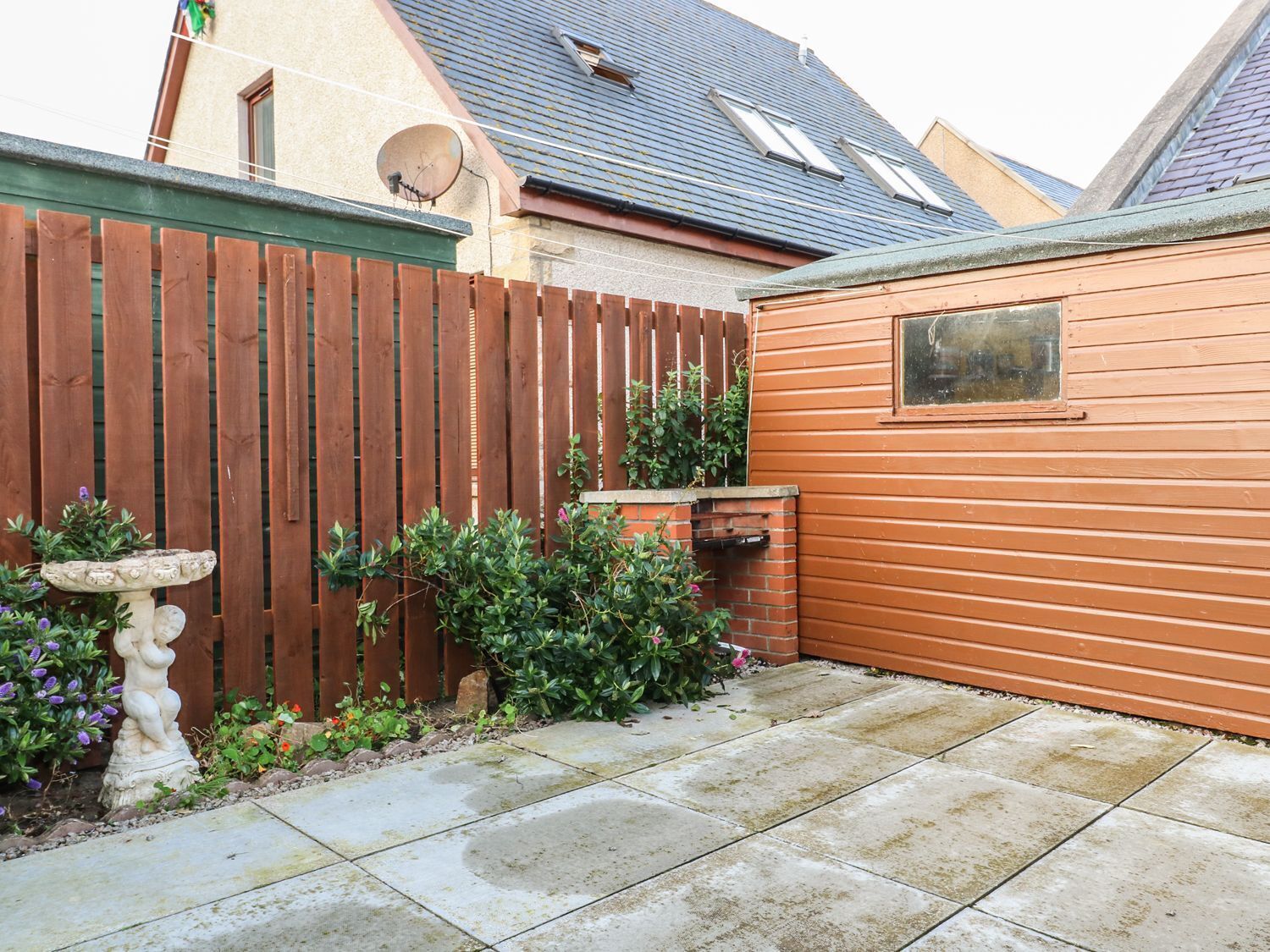 A backyard with a wooden fence, a brick barbecue, and a stone patio.