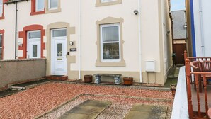 A two-story house with a white door, a small front garden with gravel, and a blue chair outside. - Harbour View (Buckie)