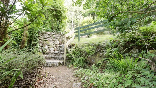 Una scala in pietra conduce a un cancello in legno, immersa in un giardino rigoglioso e verde.