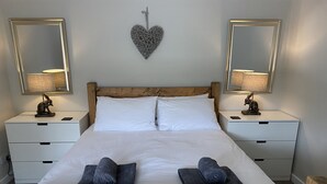 A neatly made bed with white linens, two bedside tables with lamps, and a heart-shaped decoration on the wall. - Netherraw (Hawick)