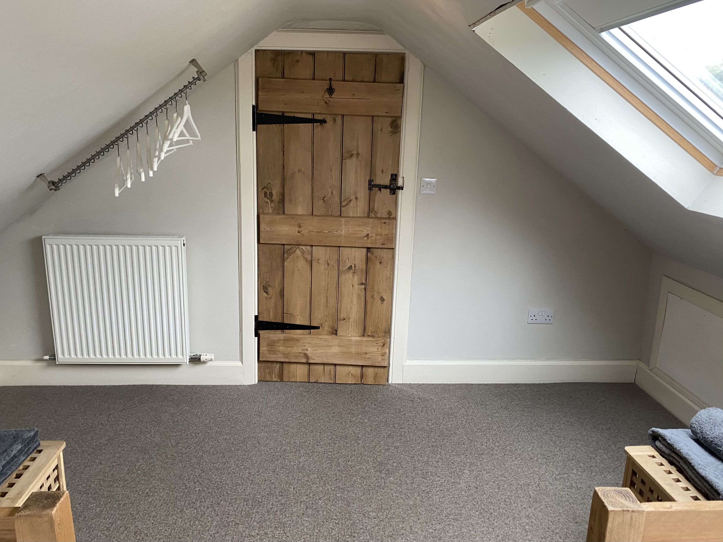 A room with a sloped ceiling, a wooden door, a white radiator, and a skylight.