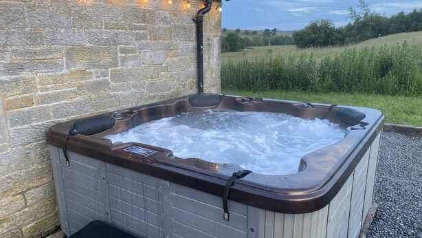 A hot tub with a control panel, a bench, and a stone wall backdrop. - Netherraw (Hawick)