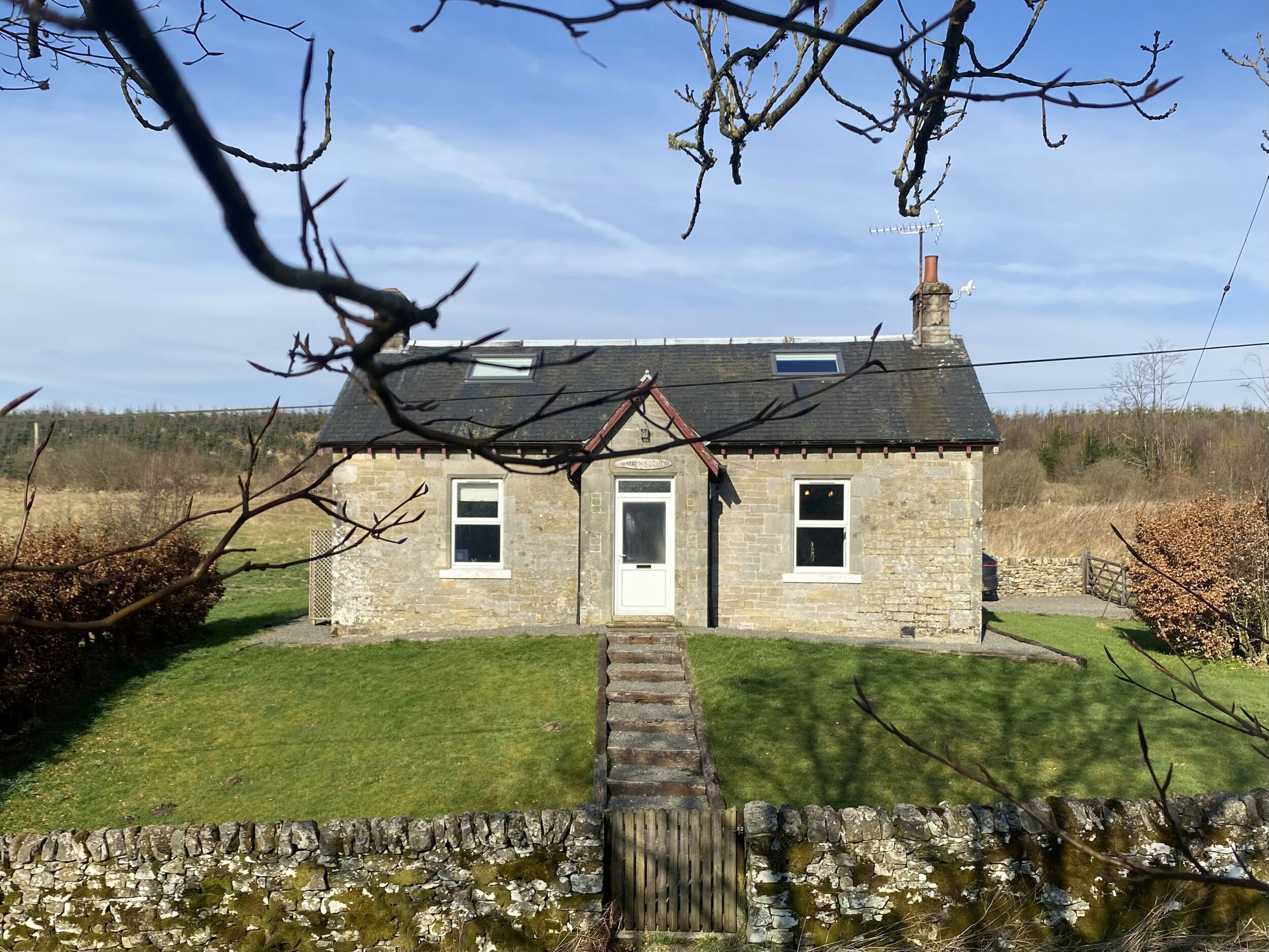 A stone house with a well-maintained lawn and a stone wall in front.
