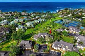 An aerial view of a coastal residential area with houses, a golf course, and a tennis court.