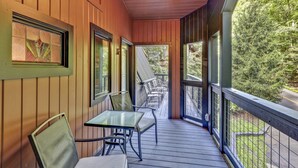 Une terrasse en bois avec des sièges extérieurs, de grandes fenêtres et une vue sur les arbres.