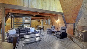 L’intérieur chaleureux d’un chalet en bois, avec un plafond en bois, une cheminée en pierre, des sièges en cuir et un coin repas.