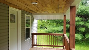 Eine Holzveranda mit Holzbalkon, einer Fußmatte und Blick auf eine grüne Landschaft.